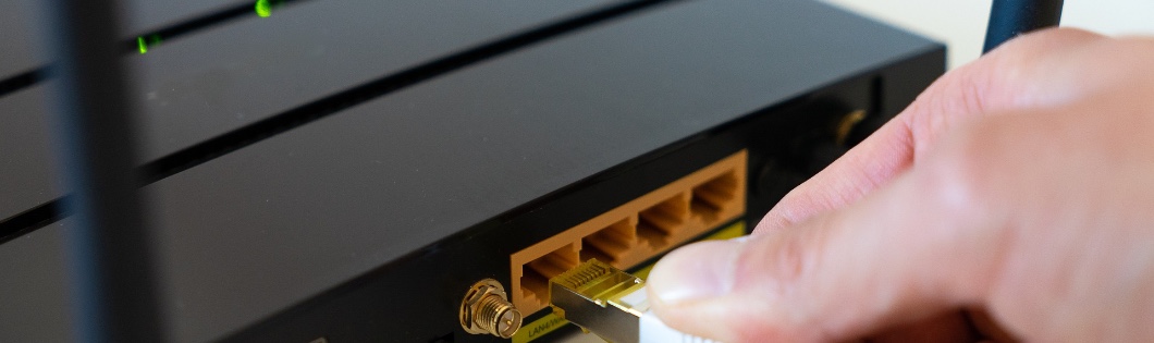 A hand plugging an ethernet cable into a router